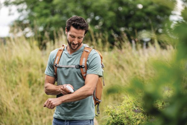 Ein sportlicher Mann mit Rucksack in der Natur wendet den Insektenstichheiler BR 10 an.