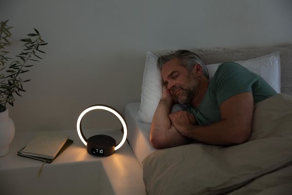 Schlafender Mann in Bett, auf Nachttisch das Beurer WL 65 Wake up + Charge, das Szene sanft beleuchtet.