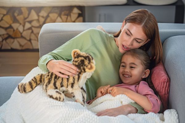 Eine Frau und ihre Tochter liegen in die Wärmezudecke HD 82 Helsinki gekuschelt auf dem Sofa und spielen mit einem Stofftier.