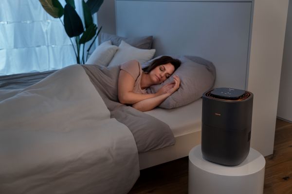 Eine Frau liegt schlafend in einem Bett, auf dem Nachttisch steht der Beurer LB 300 Plus.