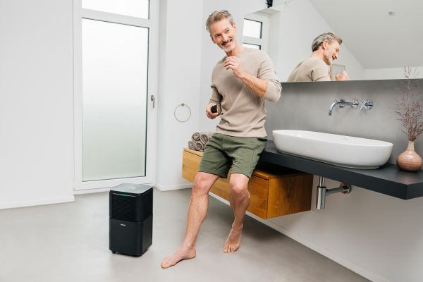 Ein Mann lehnt im Badezimmer am Waschbecken, neben ihm zu sehen ist der Luftenfeuchter LE 150.