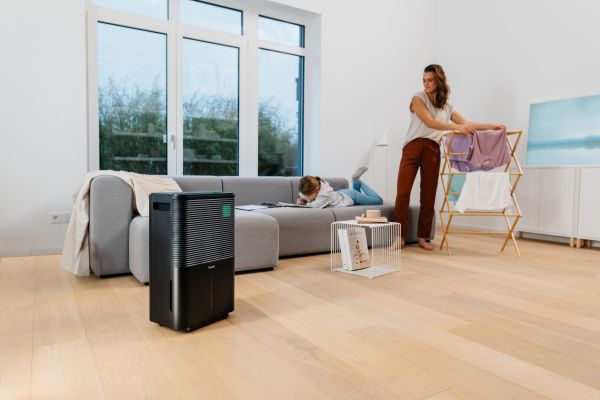 Eine Frau hängt im Wohnzimmer Wäsche auf, im Vordergrund steht der Luftenfeuchter LE 250.