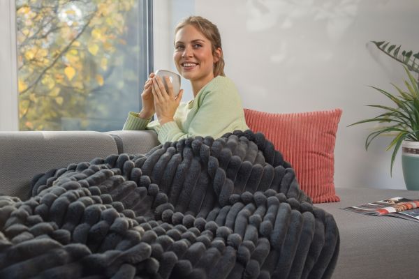 Eine Frau sitzt mit einer Tasse am Fenster, eingehüllt in die Wärmezudecke HD 82 Stockholm.