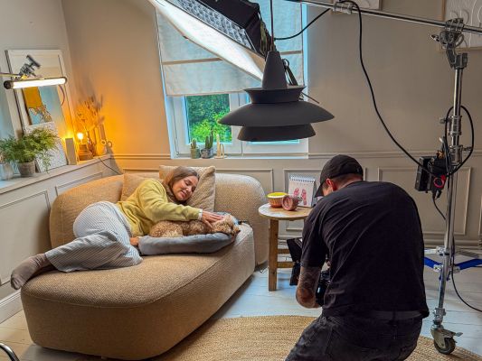 Ein Filmset ist zu sehen, mit Kameramann und einer Frau mit Hund auf einem Sofa.
