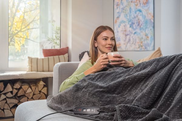 Frau liegt mit Heizdecke HD 65 auf einem Sofa