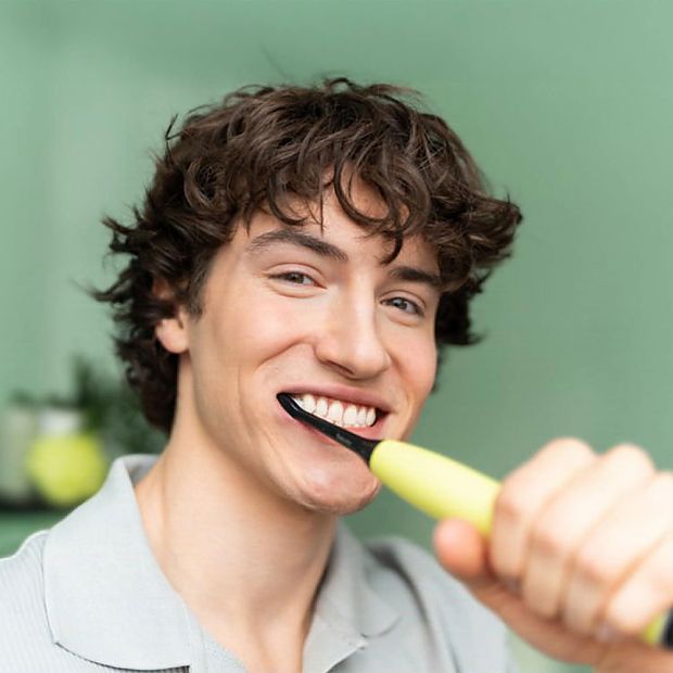 Веселый молодой человек чистит зубы в ванной с электрической зубной щеткой SC 50 Splashy Lemon GP от Beurer.