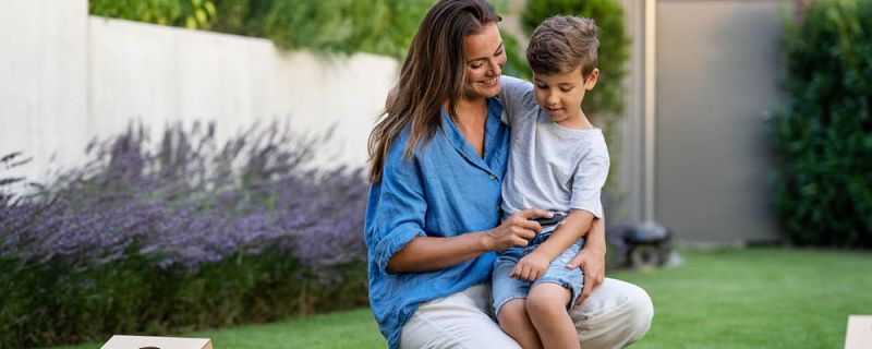 Frau im Garten hat ihren Sohn auf dem Schoß und behandelt seinen Insektenstich mit dem Beurer Insektenstichheiler BR 90