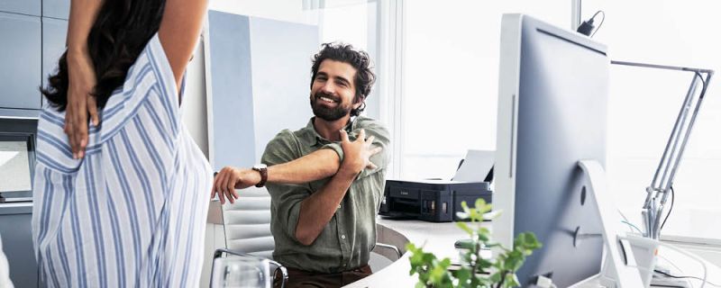 Ein Mann und eine Frau sind im Büro an ihrem Schreibtisch und führen Dehnübungen durch