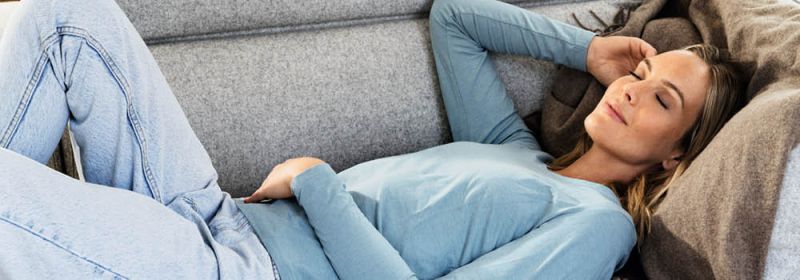 Junge Frau liegt entspannt mit geschlossenen Augen auf dem Sofa