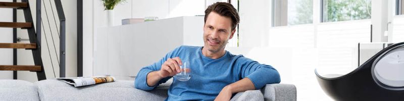 Mann mittleren Alters sitzt auf einer Couch mit einem Glas Wasser in der Hand