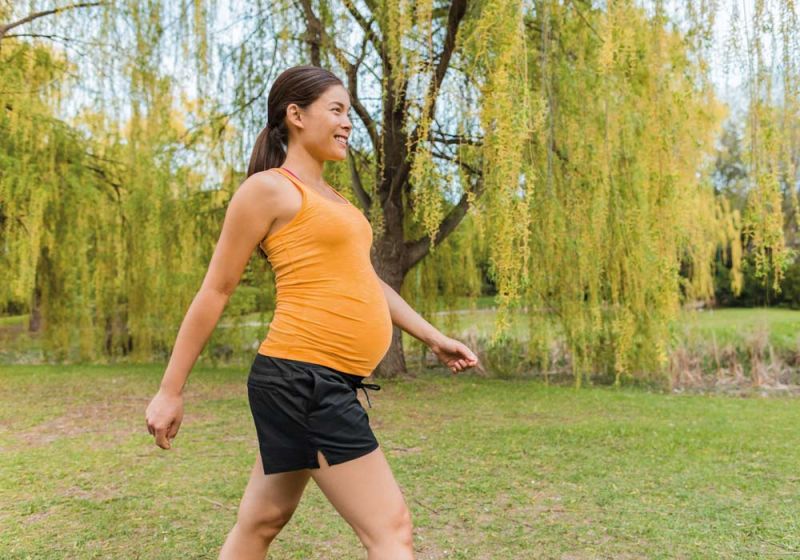 Schwangere Frau mit sportlicher Kleidung macht einen zügigen Spaziergang in der Natur