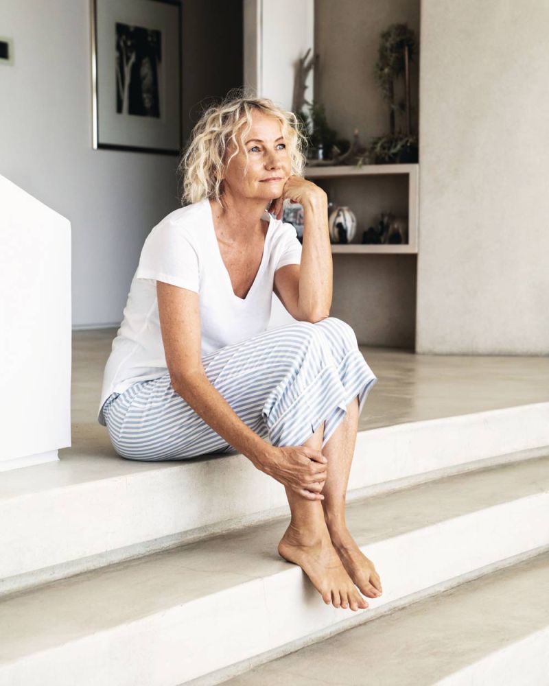 Ältere Frau sitzt zu Hause auf einer Steintreppe und blickt nachdenklich in die Weite