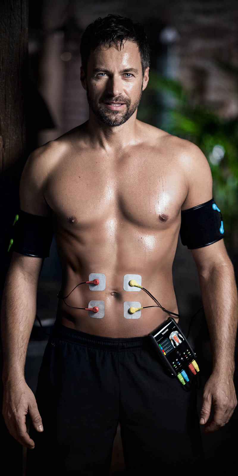 Beurer EMS Gerät EM 95 - Anwendungsbild Mann hat Elektroden am Bauch und Manschetten am Arm