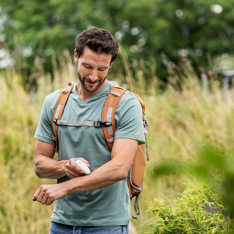Junger Mann wandert in der Natur und behandelt seinen Insektenstich am Arm mit dem Beurer Insektenstichheiler BR 10