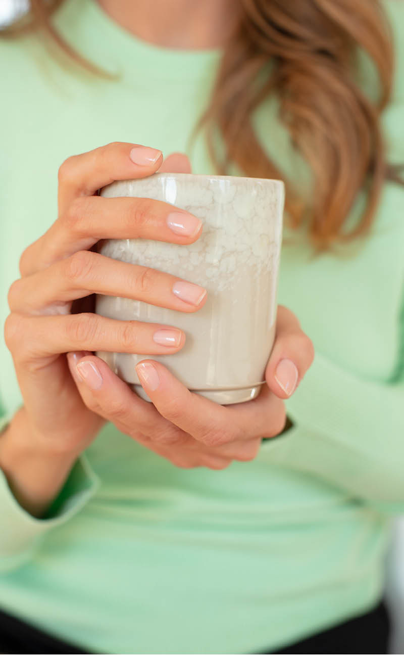 Bildausschnitt einer Frau, die eine schöne Tasse hält und man sieht ihre ordentlich gepflegten Nägel