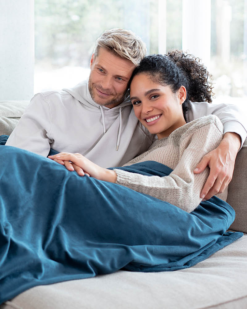 Beurer Heizdecke HD 75 cosy ocean - Anwendungsbild Pärchen liegt auf Couch unter Heizdecke