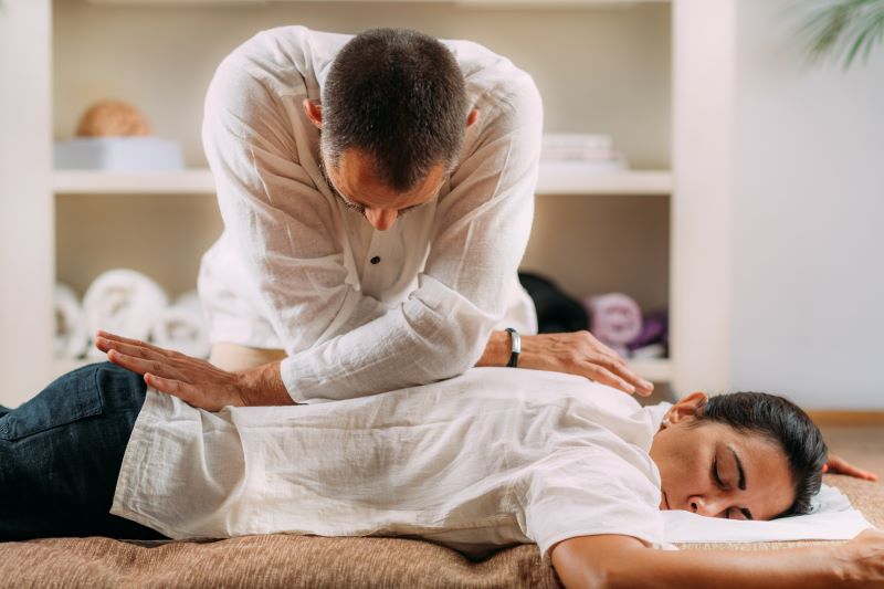 Therapeut gibt einer bekleideten Frau eine Shiatsu-Massage und übt mit seinem Körpergewicht gezielt Druck auf ihren Rücken aus