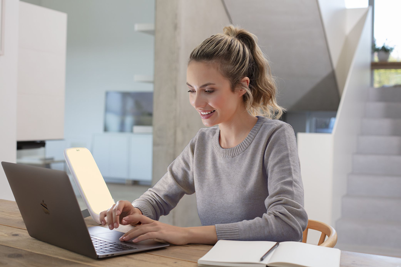 Frau arbeitet daheim am Laptop und nutzt die Beurer Tageslichtlampe TL 35