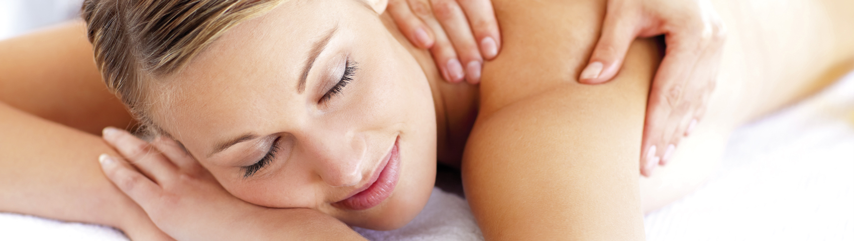 Junge Frau liegt ohne Kleidung auf dem Bauch, hat die Hände unter dem Kopf und bekommt eine Massage