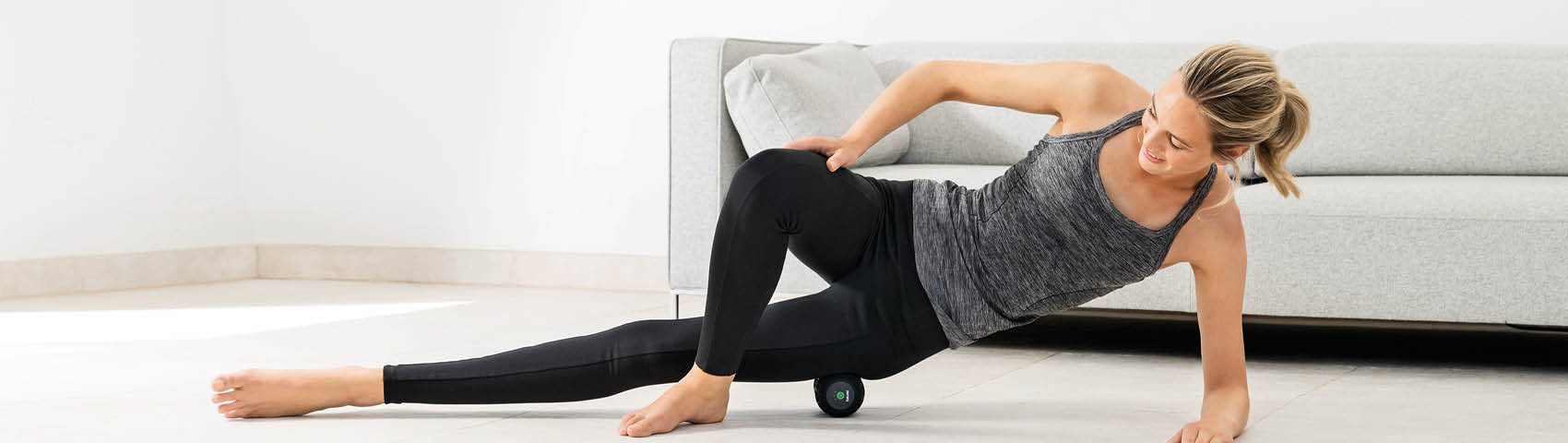 Junge Frau rollt ihren Oberschenkel über die Beurer Massagerolle MG 35, in dem sie sich auf ihren Unterarm stützt