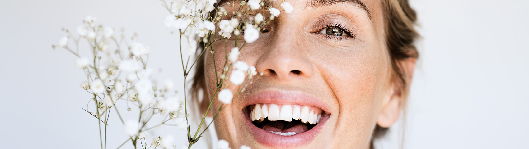 Junge Frau lächelt in die Kamera, vor ihrem Gesicht sind weiße, kleine Blumen