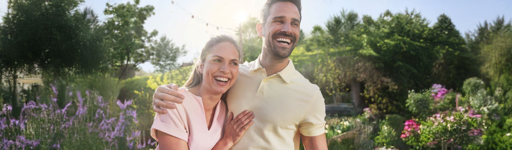 Ein junges Paar steht draußen im Garten und hält sich lächelnd im Arm
