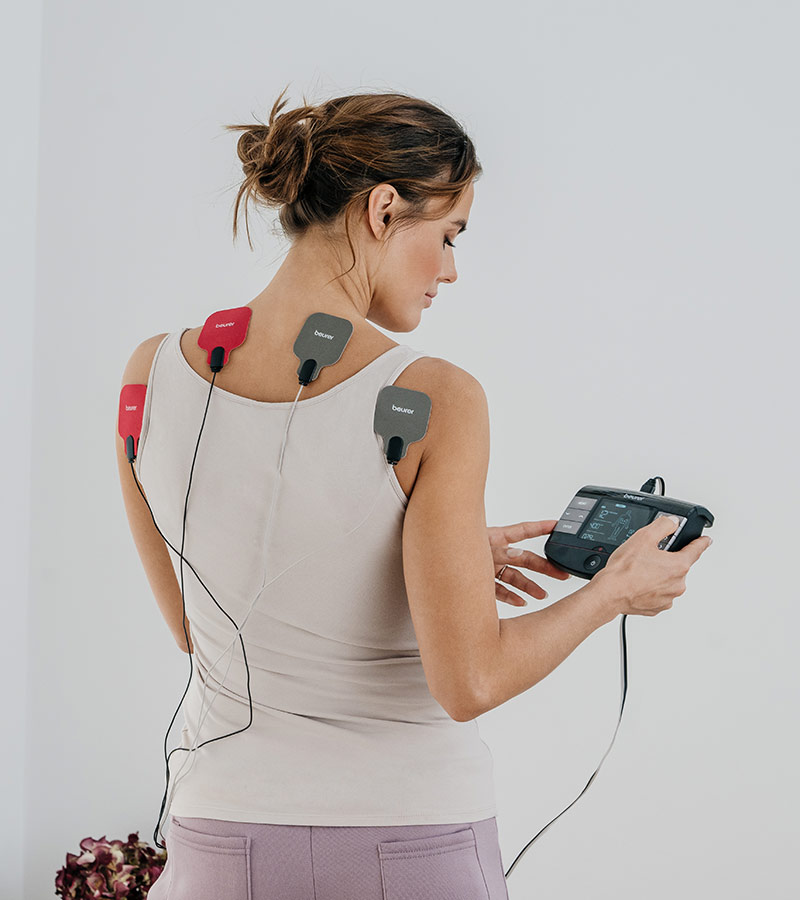Beurer EM 89 EMS/TENS Gerät - Anwendungsbild Frau nutzt Gerät am oberen Rücken
